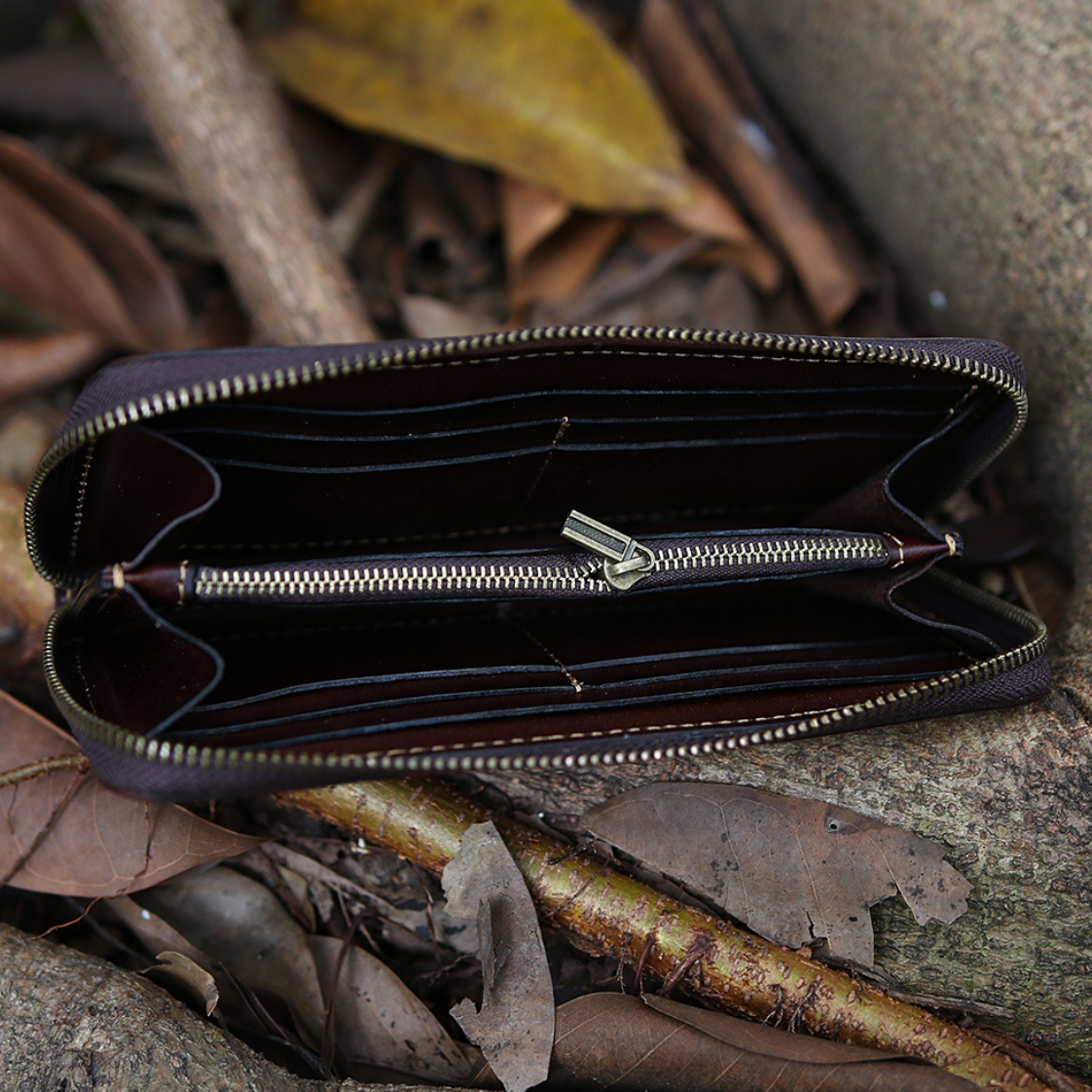 Open brown leather wallet with a zipper on a leafy ground